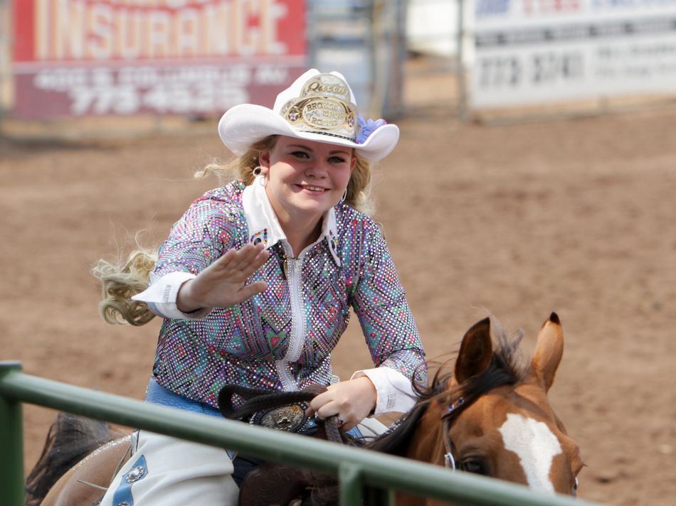 Broken Spur Rodeo Queen waves to the crowd as she rides by on her horse.