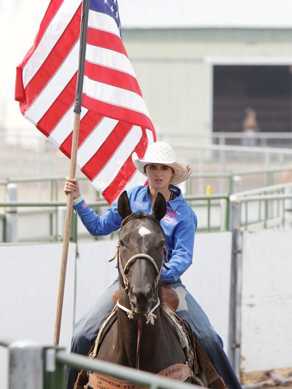 A girl holds the American Flag while riding her horse.