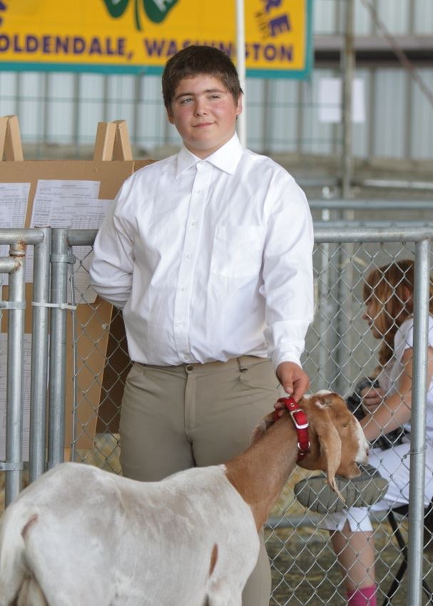 A boy stands holding his goat by the collar in the animal barn at the 2014 Klickitat County Fair.