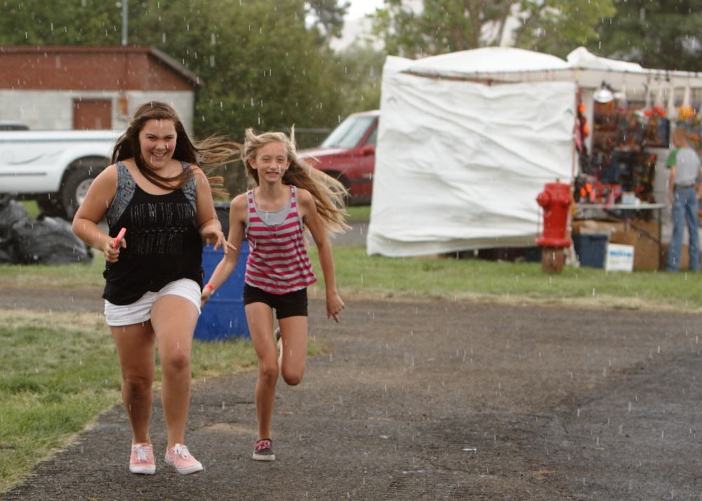 Two girls run through the rain together at the 2014 Klickitat County Fair.