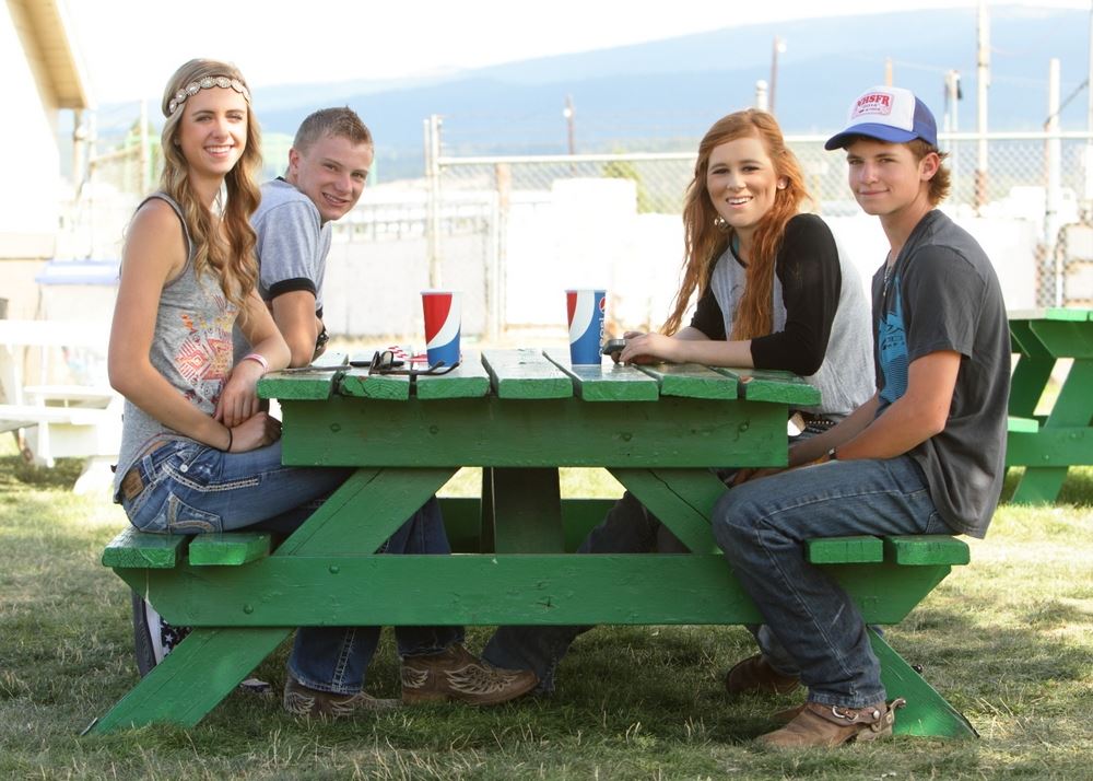 A group of teens sit together at a green picnic table.