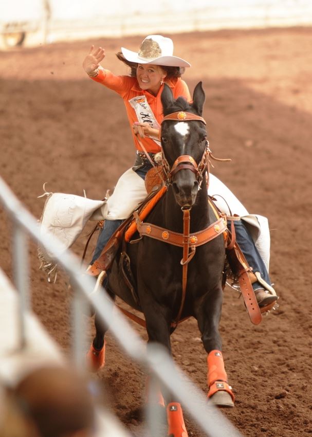 A rodeo queen rides by on her horse and waves to the crowd.