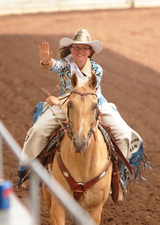 A rodeo queen waves to the crowd as she rides by on her horse.