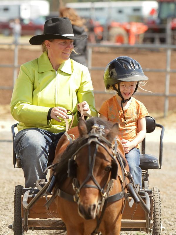 Woman and little girl ride in a cart being pulled by a pony.