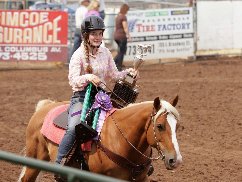 A girl riding her horse carries two trophies.
