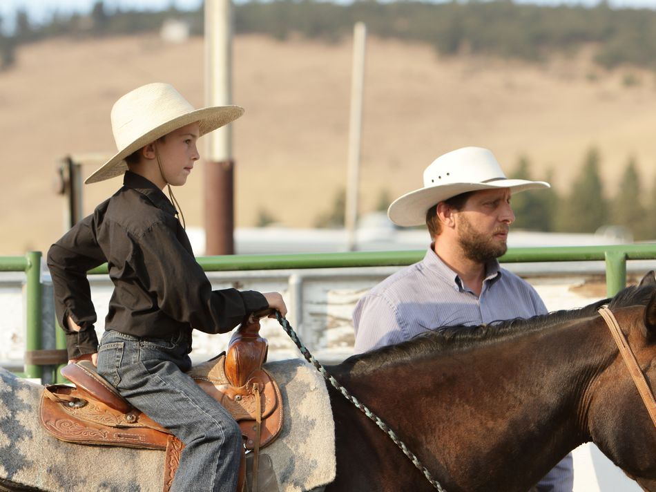 Man stands next to a little boy sitting on a horse.