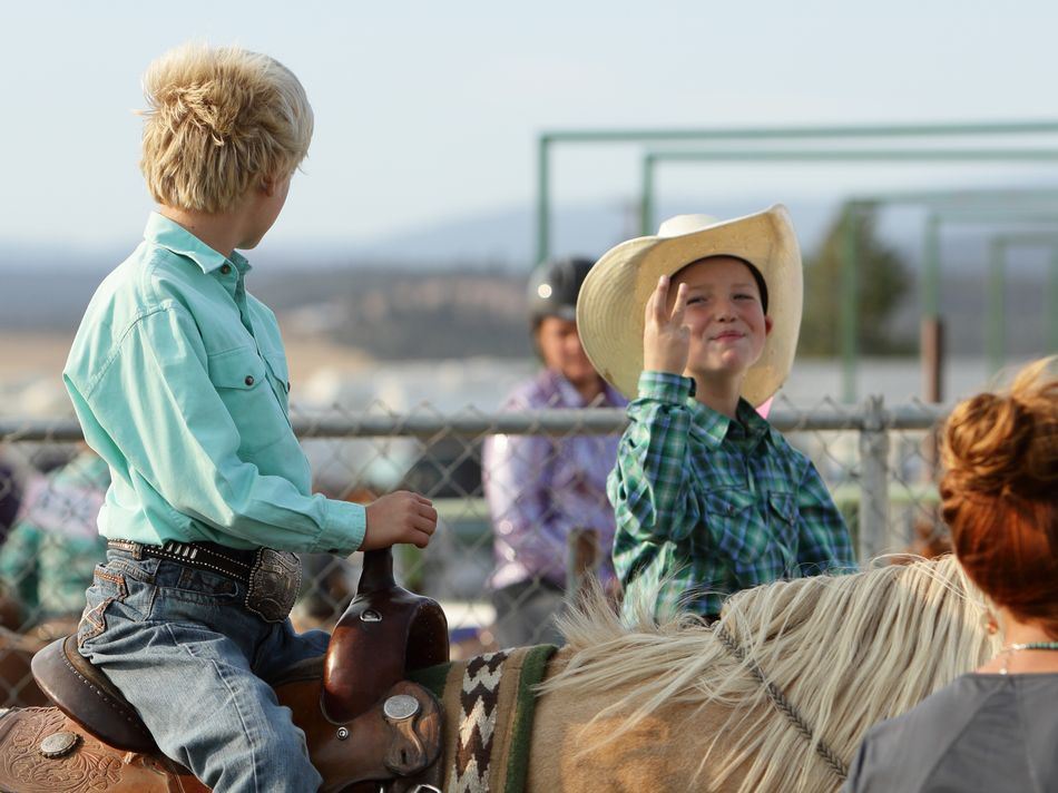 Two little boys sit on their horses next to one another.