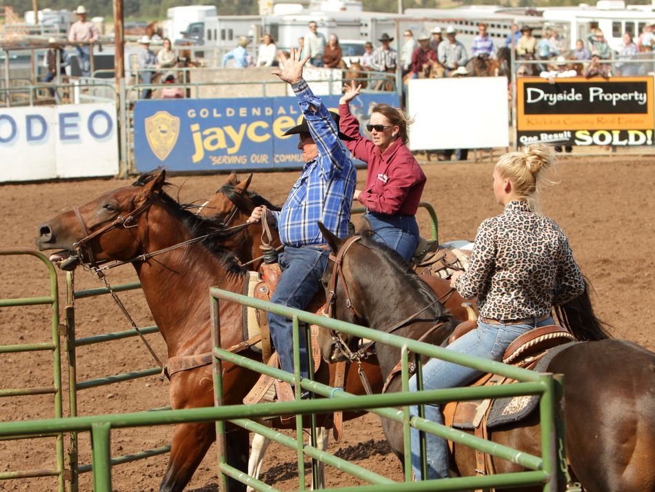 A man and a woman raise their arms in the air as they sit on their horses.